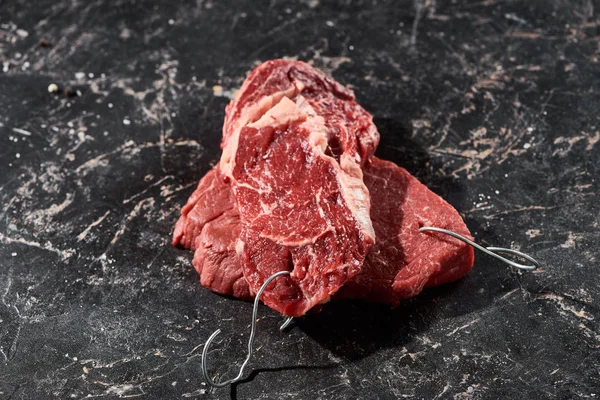 Raw beef parts with hooks on black marble surface — Stock Photo