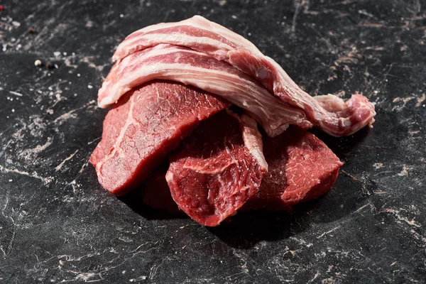 Fette di maiale crudo su bistecche di manzo su superficie di marmo nero — Foto stock