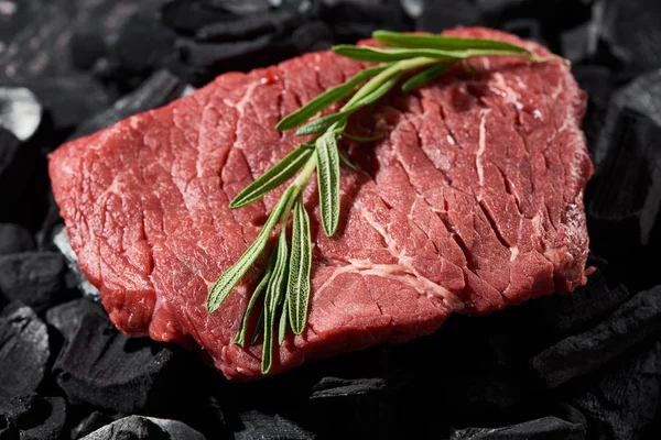 Close up view of raw beef steak with rosemary twig on charcoals — Stock Photo