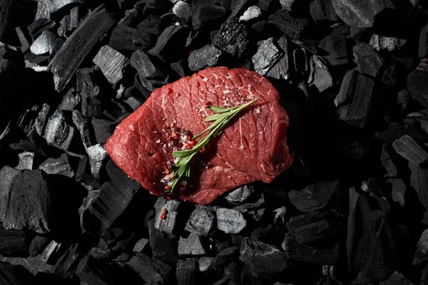 Vista dall'alto della bistecca di manzo cruda con rosmarino, sale e pepe sui carboni — Foto stock