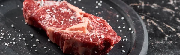 Tiro panorâmico de filé de carne crua polvilhado com sal e pimenta na superfície de madeira redonda — Fotografia de Stock