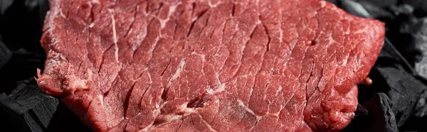 Panoramic shot of fresh raw beef fillet on coal pieces — Stock Photo