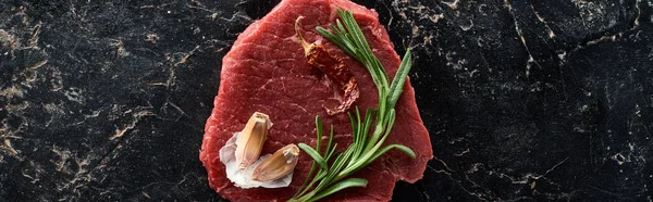 Panorama-Schuss rohes Rindfleisch mit Cayennepfeffer, Rosmarin und Knoblauch auf schwarzer Marmoroberfläche — Stockfoto