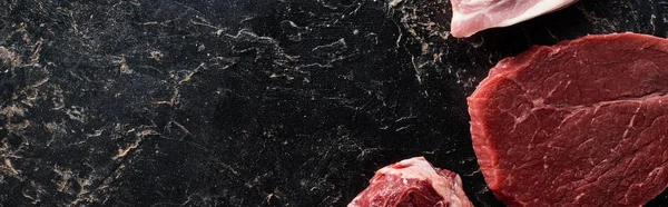 Panoramic shot of uncooked meat parts on black marble surface — Stock Photo