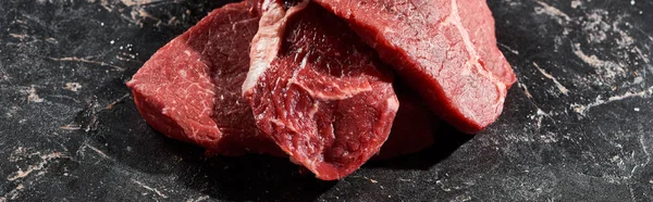 Панорамний знімок сирих шматочків яловичини один на одному на поверхні чорного мармуру — стокове фото