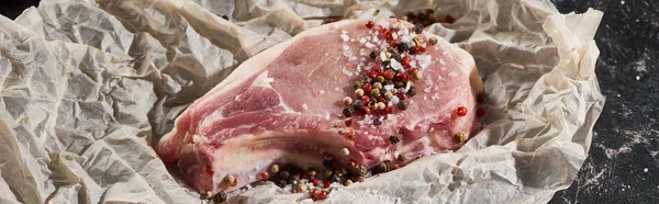 Panoramic shot of fresh raw pork steak sprinkled with salt and pepper on parchment paper — Stock Photo