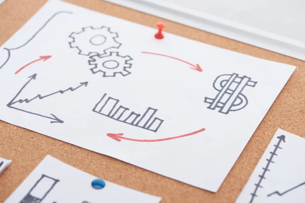 Paper card with diagrams, dollar sign and gearwheel drawing pinned on cork office board — Stock Photo