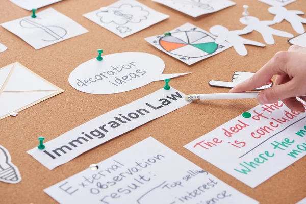 Vue recadrée de la femme pointant au crayon sur l'inscription de la loi sur l'immigration sur le panneau de liège — Photo de stock