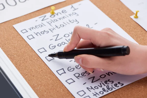 Cropped view of woman writing with black highlighter on work papers on cork board — Stock Photo