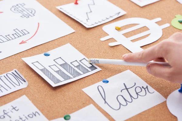 Cropped view of woman pointing with white pencil on chart on cork board — Stock Photo