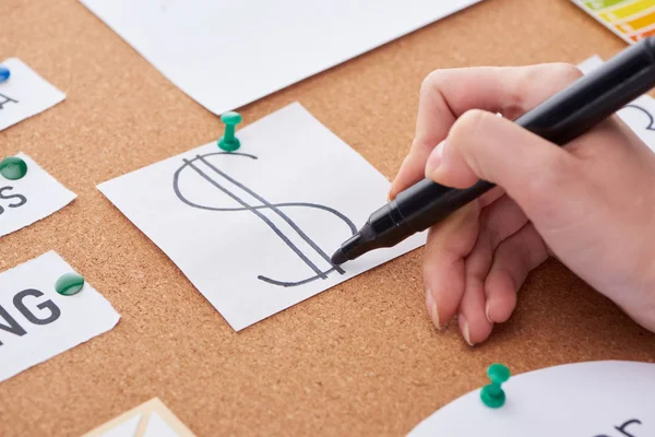 Cropped view of woman writing with black highlighter dollar sign on card pinned on cork board — Stock Photo