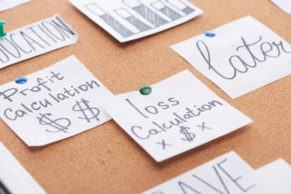 Tarjetas de papel con cálculos de pérdidas y ganancias notas fijadas en el tablero de oficina de corcho - foto de stock