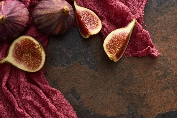 Vista superior de figos inteiros e cortados deliciosos em pano vermelho rústico no fundo de pedra — Fotografia de Stock