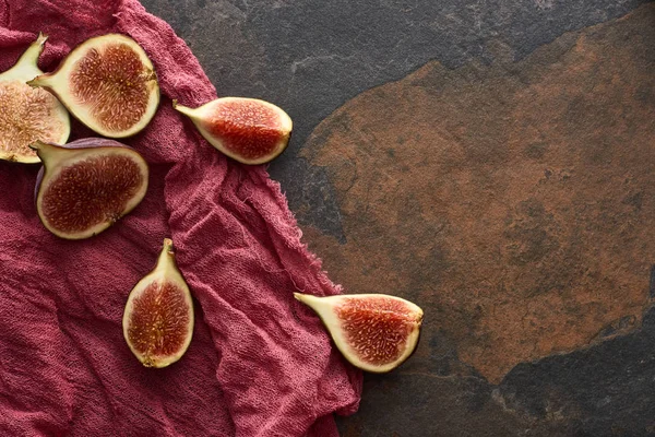 Draufsicht auf reife geschnittene köstliche Feigen auf rustikalem rotem Tuch auf steinigem Hintergrund — Stockfoto