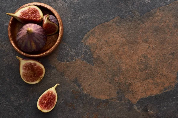 Top view of ripe whole and cut delicious figs near wooden bowl on stone background — Stock Photo