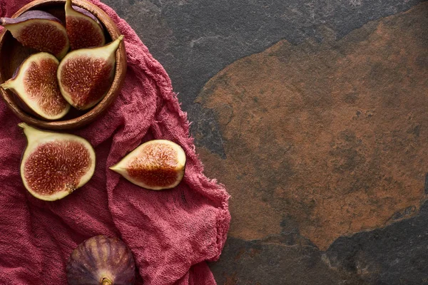 Top view of ripe cut delicious figs in wooden bowl on rustic red cloth on stone background — Stock Photo