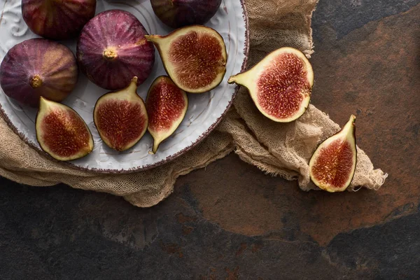 Vista superior de higos deliciosos maduros en plato blanco con paño rústico sobre fondo de piedra - foto de stock