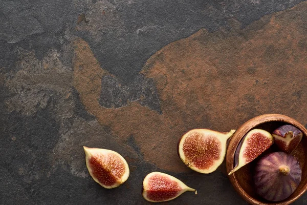 Top view of ripe whole and cut delicious figs near wooden bowl on stone background — Stock Photo