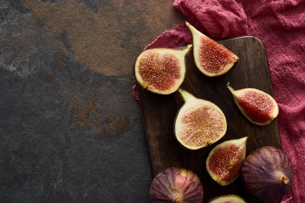Top view of ripe delicious figs on wooden cutting board near red cloth on stone background — Stock Photo