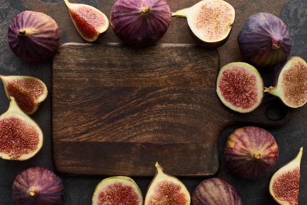 Vue de dessus de figues entières mûres et coupées délicieuses près de planche à découper vide sur fond de pierre — Photo de stock