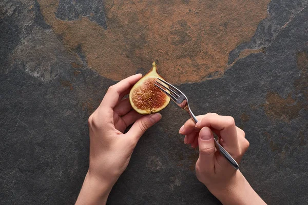 Cropped view of woman holding fork and ripe delicious fig half on stone background — Stock Photo