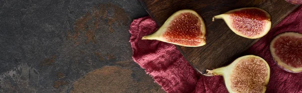 Panoramic shot of cut figs on wooden cutting board on red cloth on stone background — Stock Photo