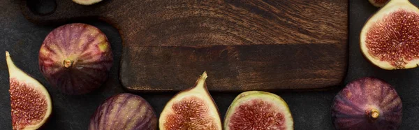 Panoramic shot of ripe figs around wooden cutting board on stone background — Stock Photo