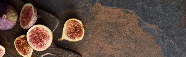 Панорамный снимок спелых инжиров на коричневой деревянной доске на каменном фоне — стоковое фото