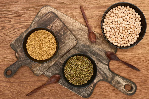 Top view of bowls with chickpea and beans on wooden cutting boards with spoons — Stock Photo