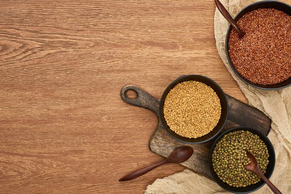 Top view of bowls with moong beans and buckwheat near spoons and canvas on wooden cutting boards — Stock Photo