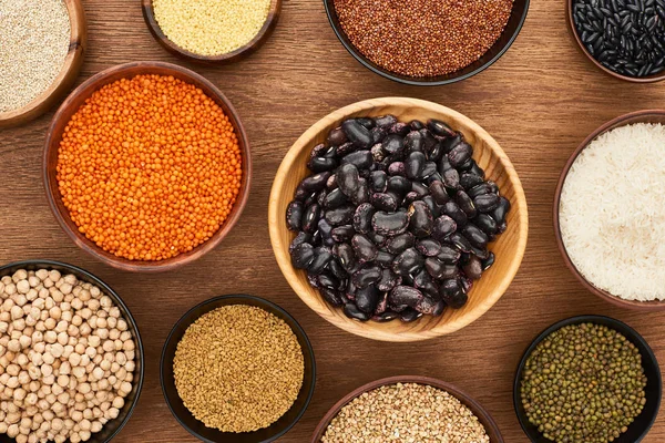 Top view of bowls with beans, white rice, red lentil, couscous and buckwheat and chickpea on wooden surface — Stock Photo