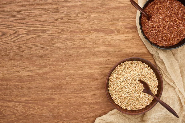 Top view of bowls with raw and roasted buckwheat on wooden surface with canvas — Stock Photo
