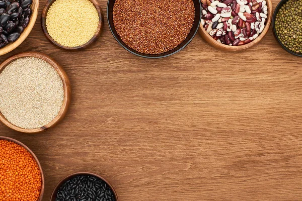 Vista dall'alto di ciotole con fagioli diversi, lenticchie rosse, couscous e grano saraceno sulla superficie di legno — Foto stock