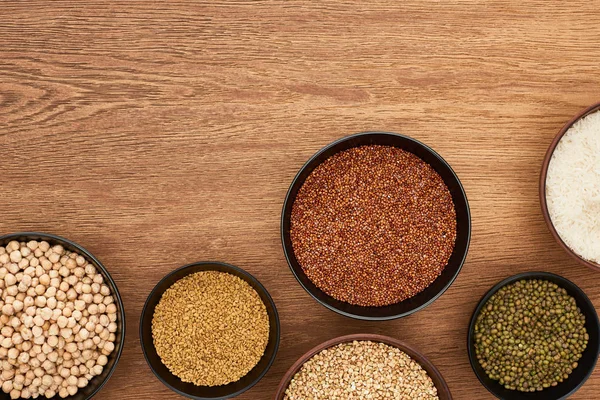 Top view of bowls with moong beans, white rice, chickpea and buckwheat on wooden surface with copy space — Stock Photo