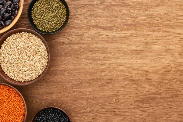 Top view of bowls with black and moong beans, buckwheat and red lentil on wooden surface — Stock Photo