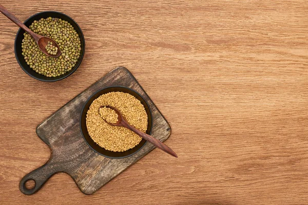 Верхний вид чаш с бобами и зерном с ложками на деревянной доске — стоковое фото