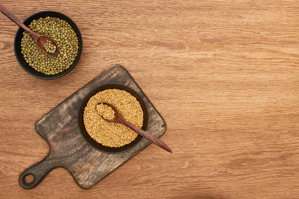 Vista superior de cuencos con frijoles y granos con cucharas en tabla de cortar de madera - foto de stock