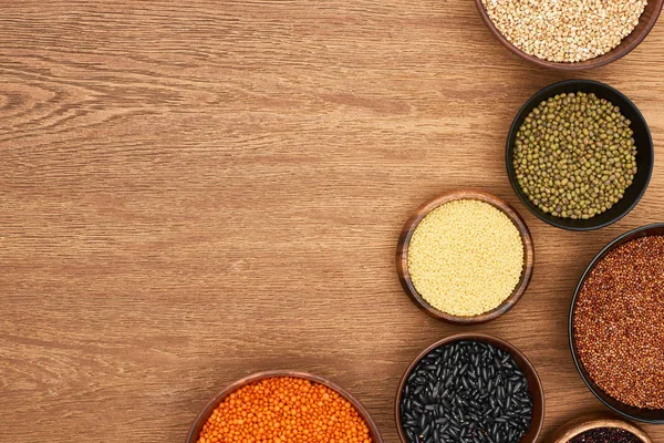 Vista superior de cuencos con frijoles negros, maash, lenteja roja, cuscús y trigo sarraceno en superficie de madera — Stock Photo