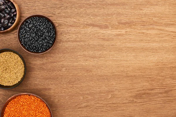 Top view of bowls with beans, red lentil, and cereal on wooden surface — Stock Photo