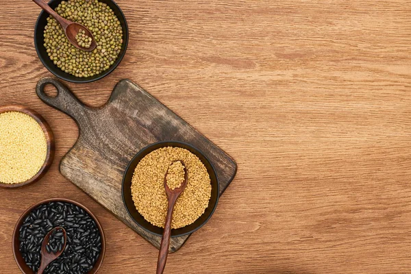 Top view of cutting board with bowls with black beans, maash, couscous and buckwheat on wooden surface — Stock Photo