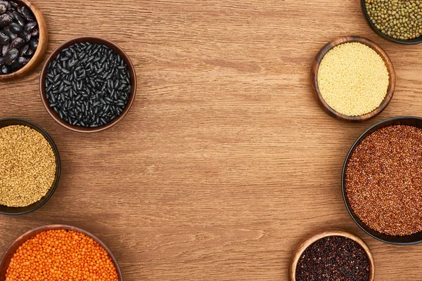 Vista superior de tigelas com quinoa, cuscuz, feijão, grão de bico e lentilha na superfície de madeira — Fotografia de Stock