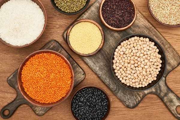 Vue du dessus des bols à grains entiers et des légumineuses sur les planches à découper en bois — Photo de stock