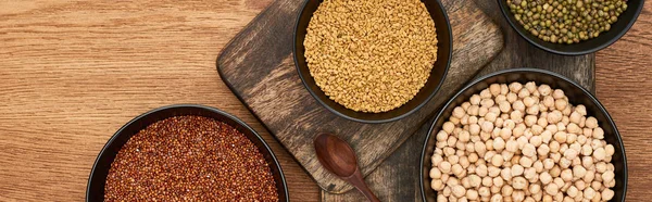 Panoramic shot of bowls with roasted buckwheat, chickpea and beans near wooden spoon on wooden cutting boards — Stock Photo