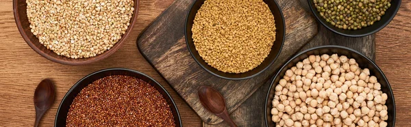 Panoramic shot of bowls with buckwheat, chickpea and beans near spoons on wooden cutting boards — Stock Photo