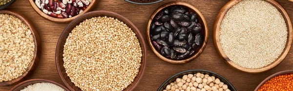 Panoramic shot of bowls with oatmeal, buckwheat, quinoa, beans and chickpea on wooden surface — Stock Photo