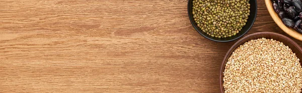 Panoramic shot of bowls with raw buckwheat and green moong beans on wooden surface — Stock Photo