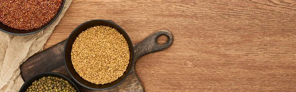 Panoramic shot of bowls with grains and beans on wooden cutting board near canvas with copy space — Stock Photo