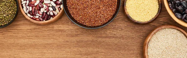 Panoramic shot of bowls with buckwheat, couscous and beans on wooden surface — Stock Photo