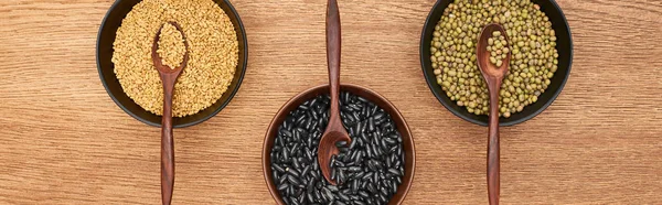 Panoramic shot of bowls with diverse beans and grains with spoons on wooden surface — Stock Photo