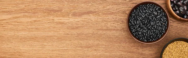 Panoramic shot of bowls with black beans ang grains on wooden surface with copy space — Stock Photo